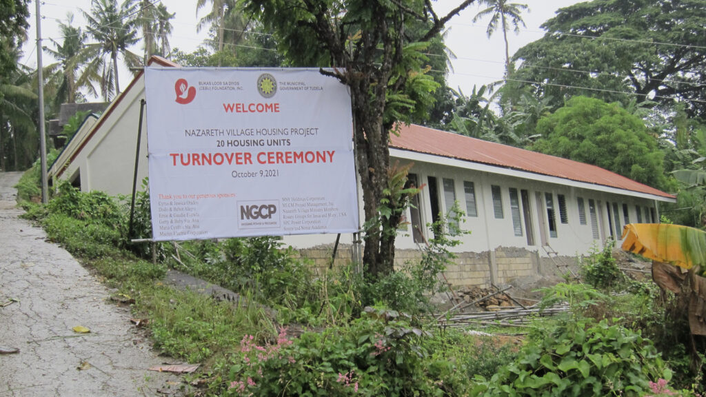 A photo of one of the finished housing unit with a tarpaulin sign saying "Turnover Ceremony"